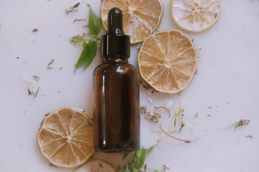 Product photo of a glass dropper bottle containing natural anti aging serum sat against an aromatic milk bath containing dried citrus and herbs