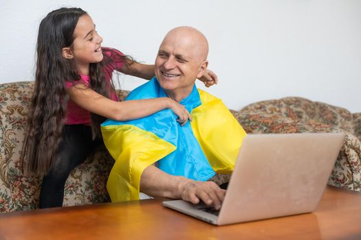 Grandfather and granddaughter with laptop and flag of Ukraine.