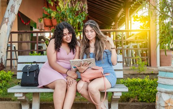 Two pretty girls reading on a bench, two pretty women reading a book on a bench, girls sitting on a bench reading