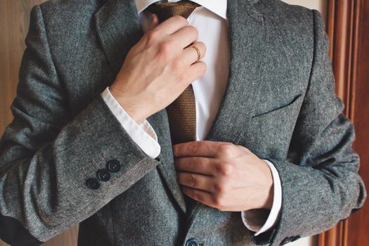 Man in smart suit wearing wedding ring adjusting tie