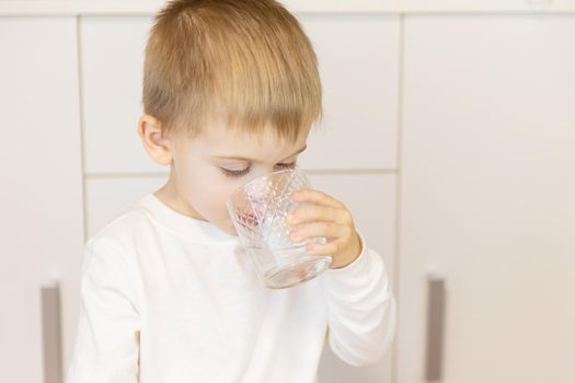 The child drinks water from a glass. Selective focus.