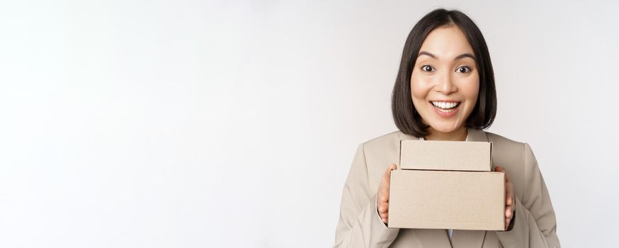 Enthusiastic asian businesswoman, giving customer order boxes, standing against white background. Copy space