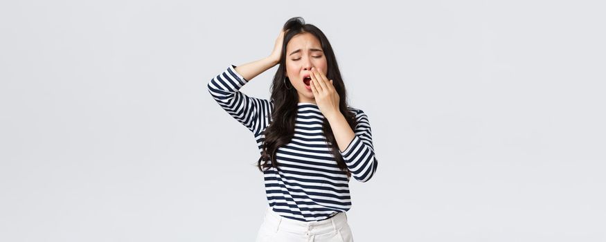 Lifestyle, people emotions and casual concept. Sleepy tired woman working late in office, close eyes and yawning, want go bad. Asian girl woke up early, need coffee, stand white background.