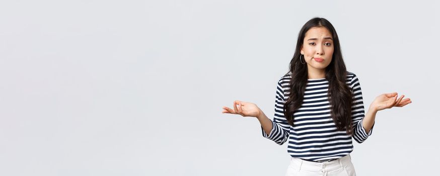 Lifestyle, beauty and fashion, people emotions concept. Smiling cute clueless girl dont have idea, no answer, shrugging with hands spread sideways, standing white background.