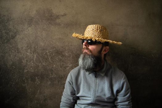 A man with a beard in a straw hat against a wall background