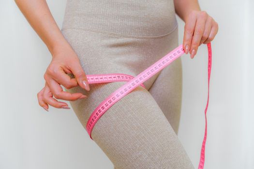 Cropped view of slim woman measuring her leg with tape measure at home, close-up. An unrecognizable European woman checks the result of a weight loss diet or liposuction indoors. Healthy lifestyle