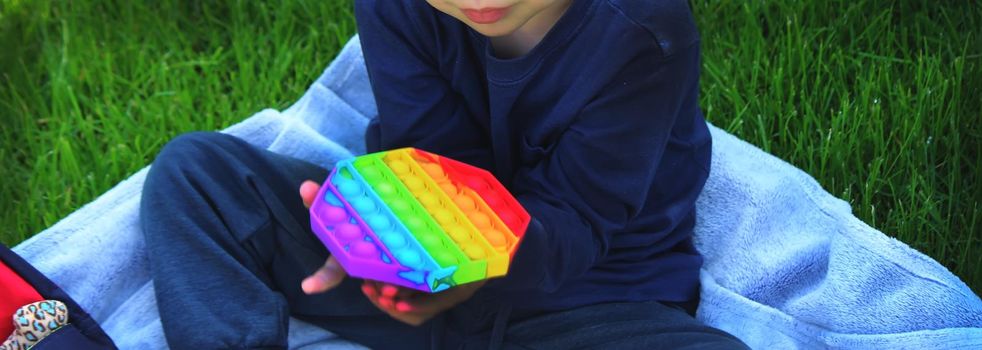 Pop it silicone anti-stress toy. The child plays on the grass. New trend Selective focus. Nature