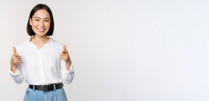 Its you congrats. Smiling attractive asian woman, businesswoman pointing fingers at camera with pleased face, complimenting, inviting you, standing over white background.