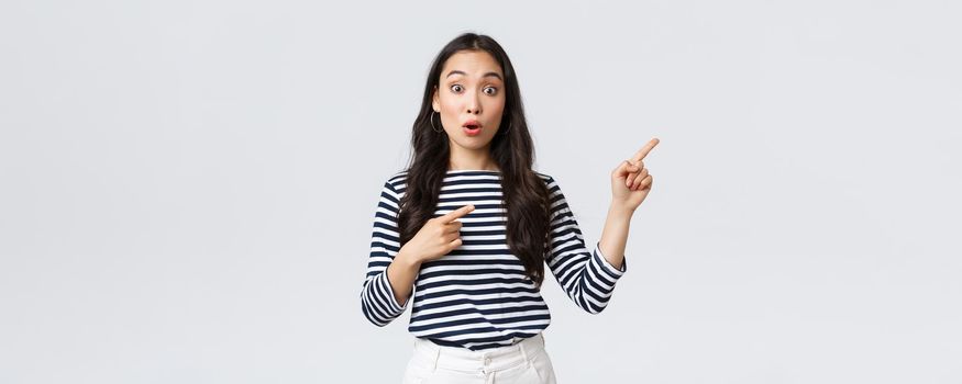 Lifestyle, beauty and fashion, people emotions concept. Surprised and intrigued attractive asian woman customer pointing fingers upper right corner, say wow amazed, found awesome product.