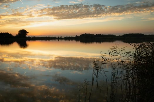 Reflection of clouds in the lake water after sunset, summer view