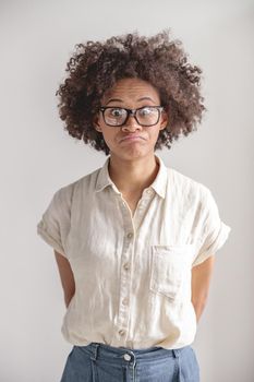 Portrait of confused African American woman in glasses posing in studio, isolated on grey background