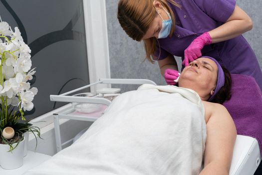 The beautician squeezes the brightening serum into the skin of the client's face from the syringe to reduce redness and wrinkles