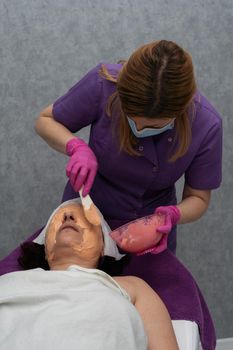 A professional algae mask is applied to the client's face with a spatula