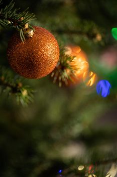 A shiny ornament in the shape of a round Christmas ball attached to a Christmas tree on a Christmas background with cork lights.