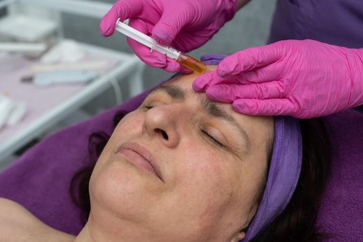 The beautician squeezes the brightening serum into the skin of the client's face from the syringe to reduce redness and wrinkles