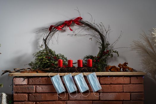 Red brick fireplace. Protective masks are hanging. Four red candles complement the Christmas decorations on the mantelpiece.