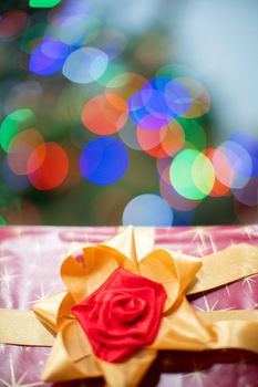 A large red bow on a Christmas gift. A decorative box with a Christmas gift in the background with cork lights.