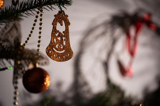 A shiny bell-shaped ornament attached to a Christmas tree in the background with a round wreath.