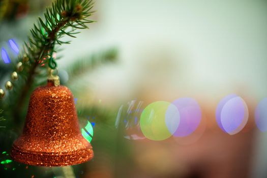 A shiny bell-shaped ornament attached to a Christmas tree in the background with cortical lights.