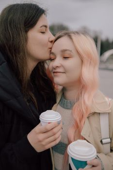 Young ukrainian lesbian couple kissing each other at the street with coffee pink hair