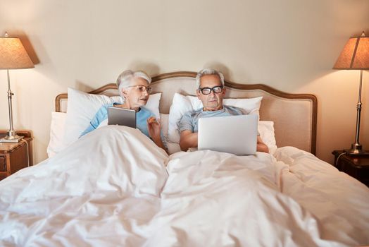 Cropped shot of a senior couple sitting in bed together and using technology in a nursing home.