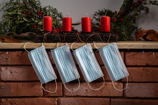 Red brick fireplace. Protective masks are hanging. Four red candles complement the Christmas decorations on the mantelpiece.