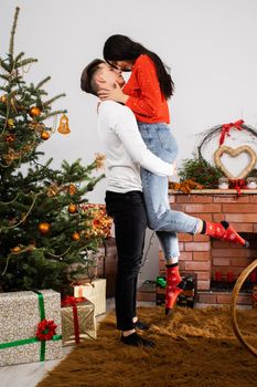 The fiance lifted his partner up in a fit of joy. Lovers flirt in a decorated living room at home. December Christian holidays.