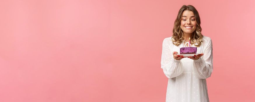 Holidays, spring and party concept. Portrait of dreamy, happy birthday girl feeling excitement and joy celebrating b-day, biting lip and smiling as making wish blowing candle on cake.