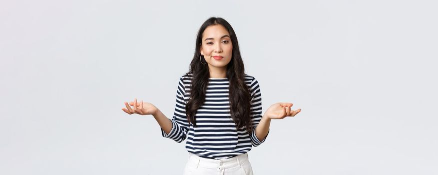 Lifestyle, beauty and fashion, people emotions concept. Clueless and unbothered asian woman shrugging with hands spread sideways and unaware smirk, standing white background.