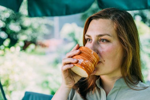 a young girl in the summer drinks hot tea, sitting on a swing, in her yard, tea helps in the heat best of all