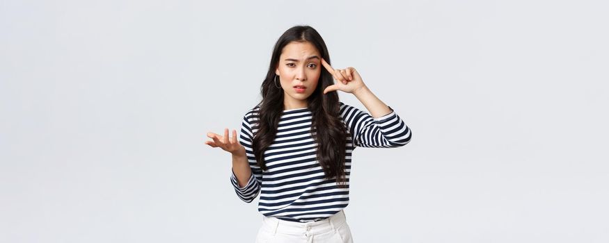 Lifestyle, people emotions and casual concept. Disappointed and annoyed young asian woman scold person making stupid mistake, roll finger over temple and raise hand in dismay.
