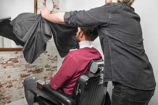 Hipster client covered with cape waiting for haircut at barbershop. High quality photo