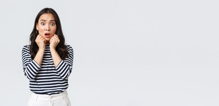 Lifestyle, people emotions and casual concept. Scared worried asian girl in striped shirt, gasping looking alarmed, got in trouble, find out shocking truth, standing white background.