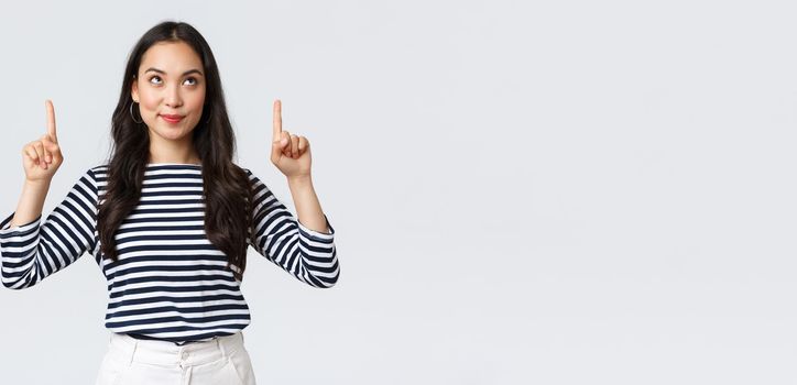 Lifestyle, people emotions concept. Excited good-looking asian girl smiling pleased as found excellent product, pointing fingers up at advertisement and looking satisfied, recommend promo.