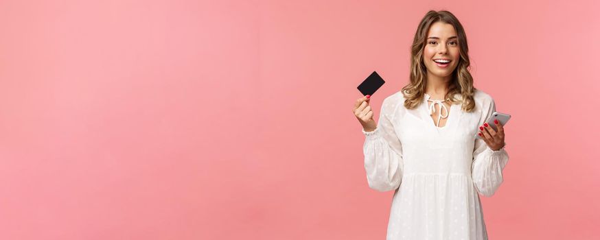 Portrait of carefree young pretty blond woman using mobile phone to pay for online purchase, holding credit card and smiling happy camera, shopping internet, download smartphone app.