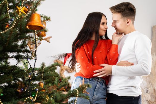 The fianc e hugged his fianc e and looks her straight in the eyes as he stands by the decorated Christmas tree. December Christian holidays.