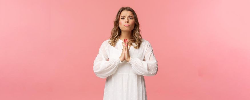 Portrait of hopeful clingy girlfriend, blond girl begging for favour in white dress over pink background, sobbing make cute eyes, pleading or praying, say please, want something badly.