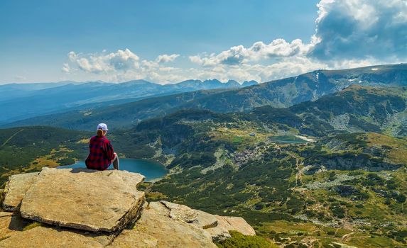 A young girl enjoys a beautiful view sitting on the rock from the top. Travel in the mountains.