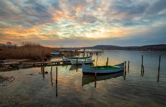 The tranquil afternoon on a lake with a wooden pier and boats at colorful sky.