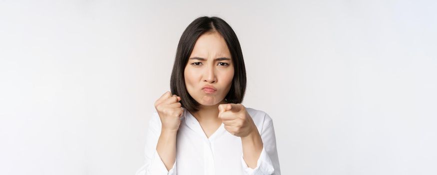 Close up of angry young woman clench fists, ready for fight, fighting, standing over white background.