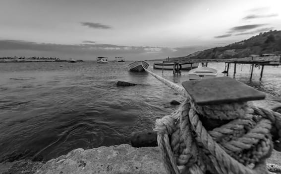 Black and white landscape with selective focus on rope anchoring fishing boat at the pier.