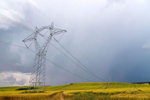 High voltage electric pole and transmission lines over golden wheat field with road