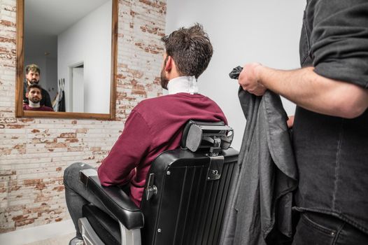 Hipster client covered with cape waiting for haircut at barbershop. High quality photo