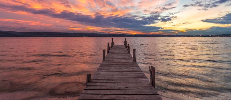 Banner of colorful sunset at a lake coast at a wooden pier.