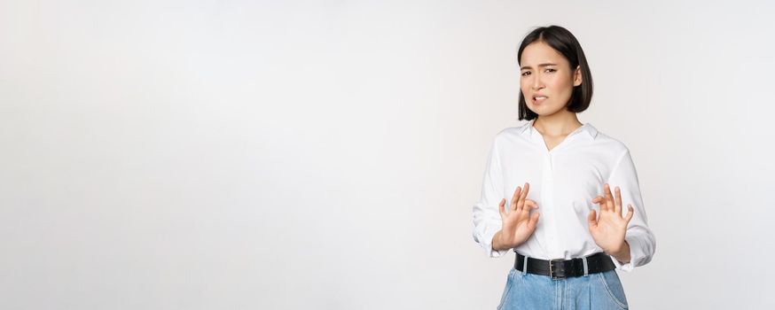 No thank you. Young disgusted asian woman declining proposal, shaking hands and step back, looking with dislike, rejecting offer, standing over white background.