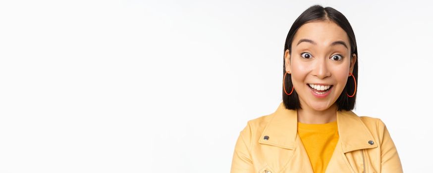 Close up of impressed asian girl, say wow, looking amazed at camera, standing in casual clothes over white background. Copy space