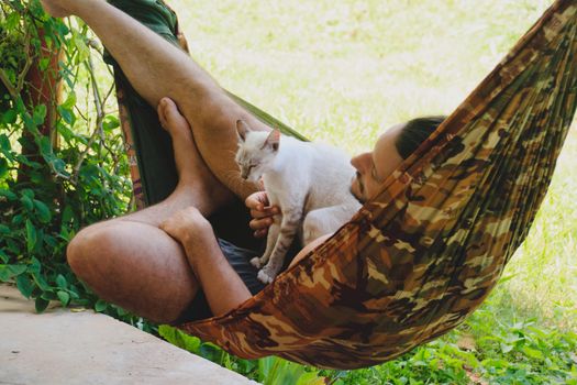 A man relaxing in the hammock with his pet siamese cat