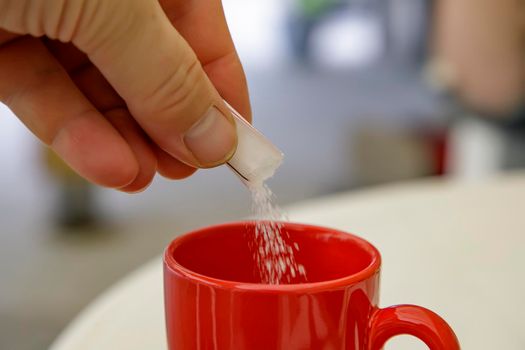 hand putting sugar in a cup of coffee or tea. Close