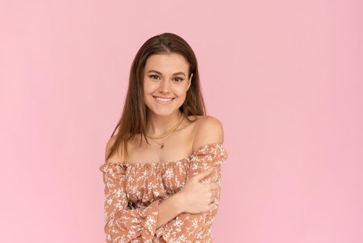 Pretty young woman in a beige dress on a pink background with copy space. Summer concept