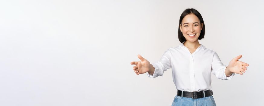 Image of smiling asian woman welcoming guests clients, businesswoman stretching out open hands, greeting, standing over white background.